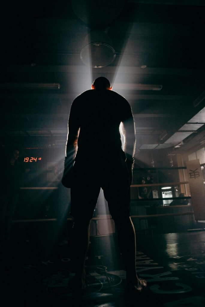 Silhouette of a boxer in a gym, illuminated by dramatic beams of sunlight, creating a powerful visual impact.
