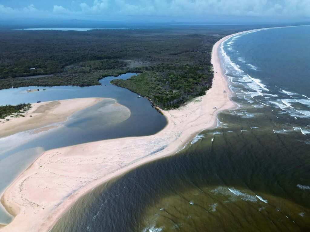 A breathtaking aerial shot capturing a beach, forest, and coastline with waves crashing along the shore.